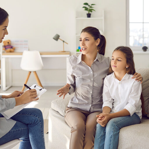 Mother sitting on sofa with sad preteen kid and talking to counseling therapist. Parent and psychologist discuss behaviour problem, peer interaction issue, ways to support child in difficult situation