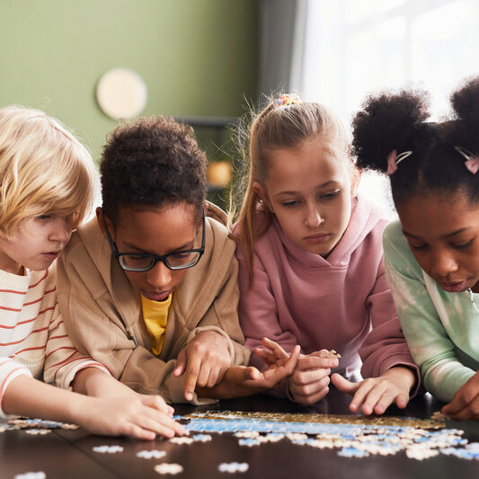 Front view portrait of diverse group of children playing with puzzle game indoors together